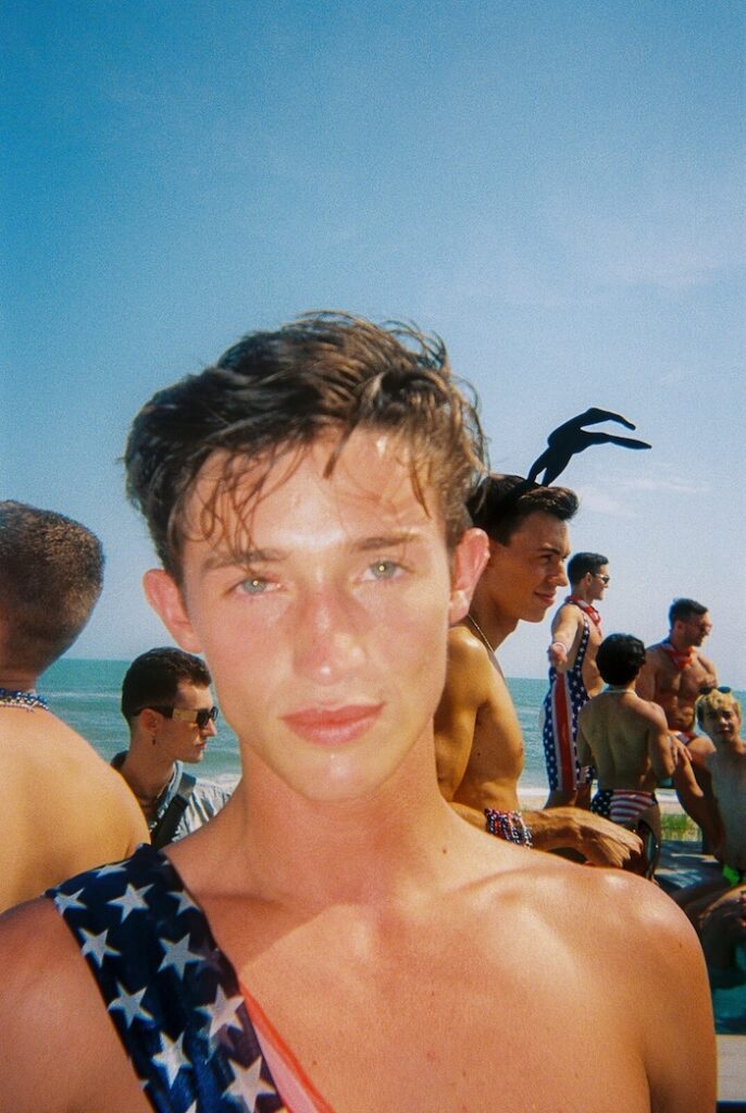 Portrait of a person at a summer beach gathering in Fire Island Pines with the ocean in the background.
